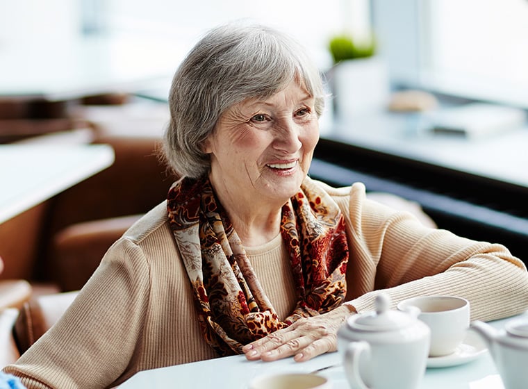 senior woman drinking coffee at diner while smiling