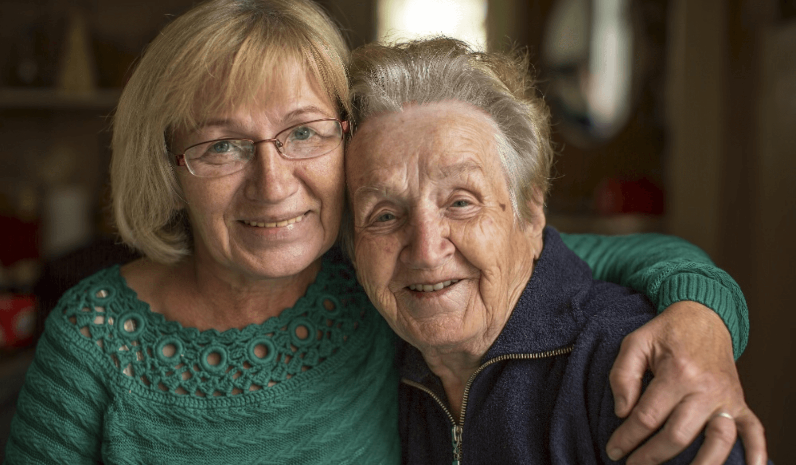 Two women smiling and embracing each other indoors.