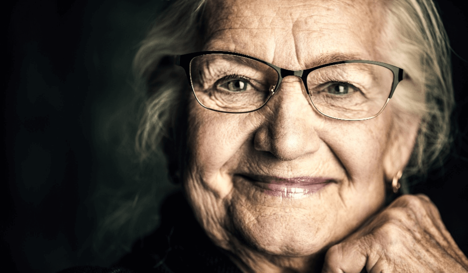 Close-up portrait of an elderly person with glasses, smiling warmly.